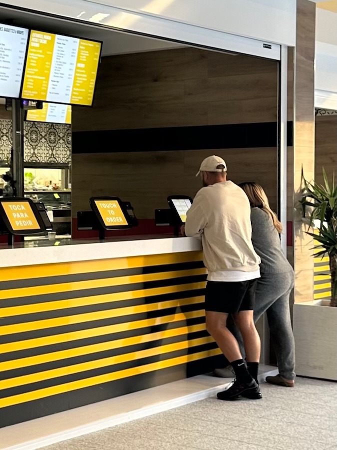 Clientes haciendo su pedido en quioscos de autoservicio de un restaurante de servicio rápido